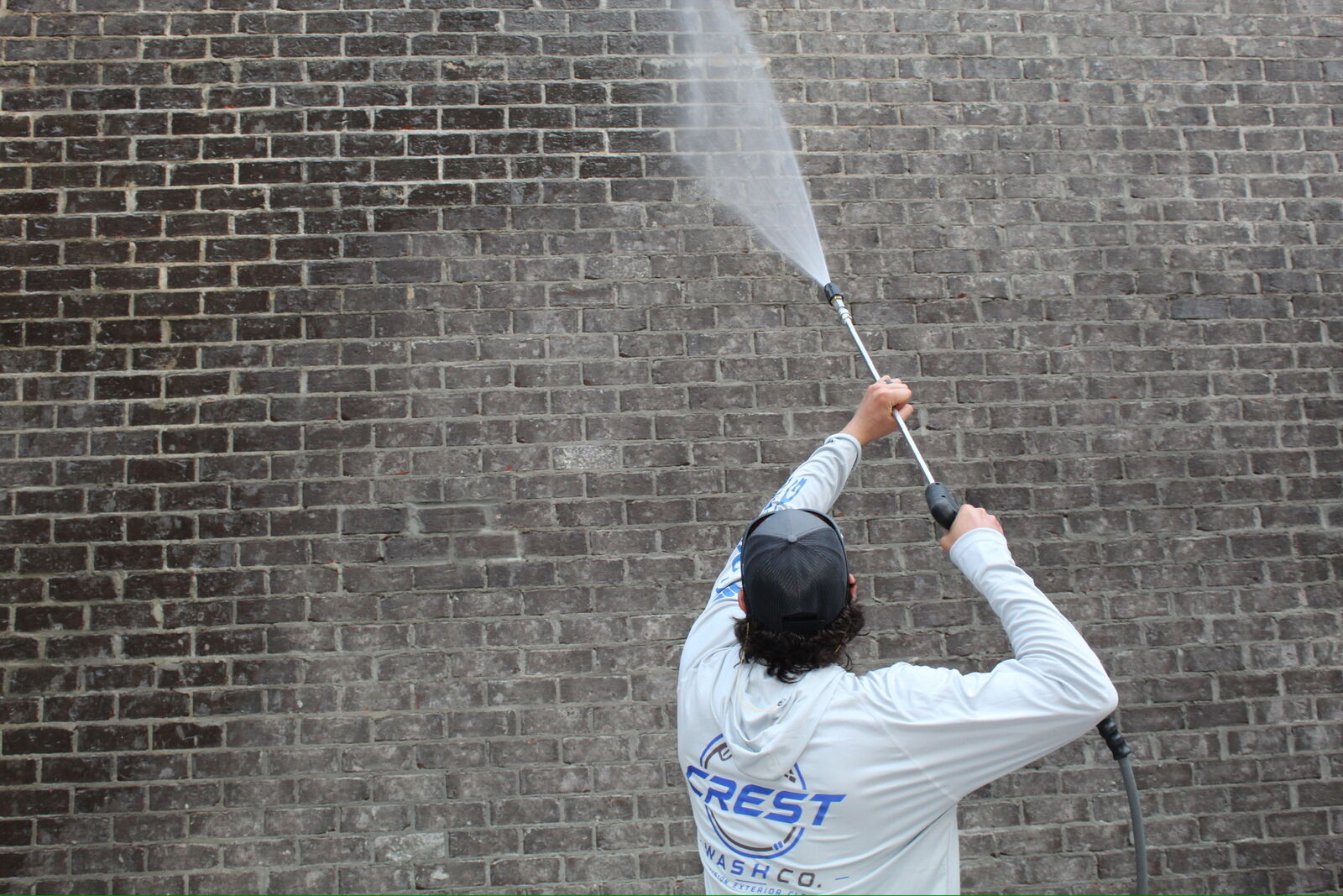 Pressure washing a dark brick wall with a high-reach lance